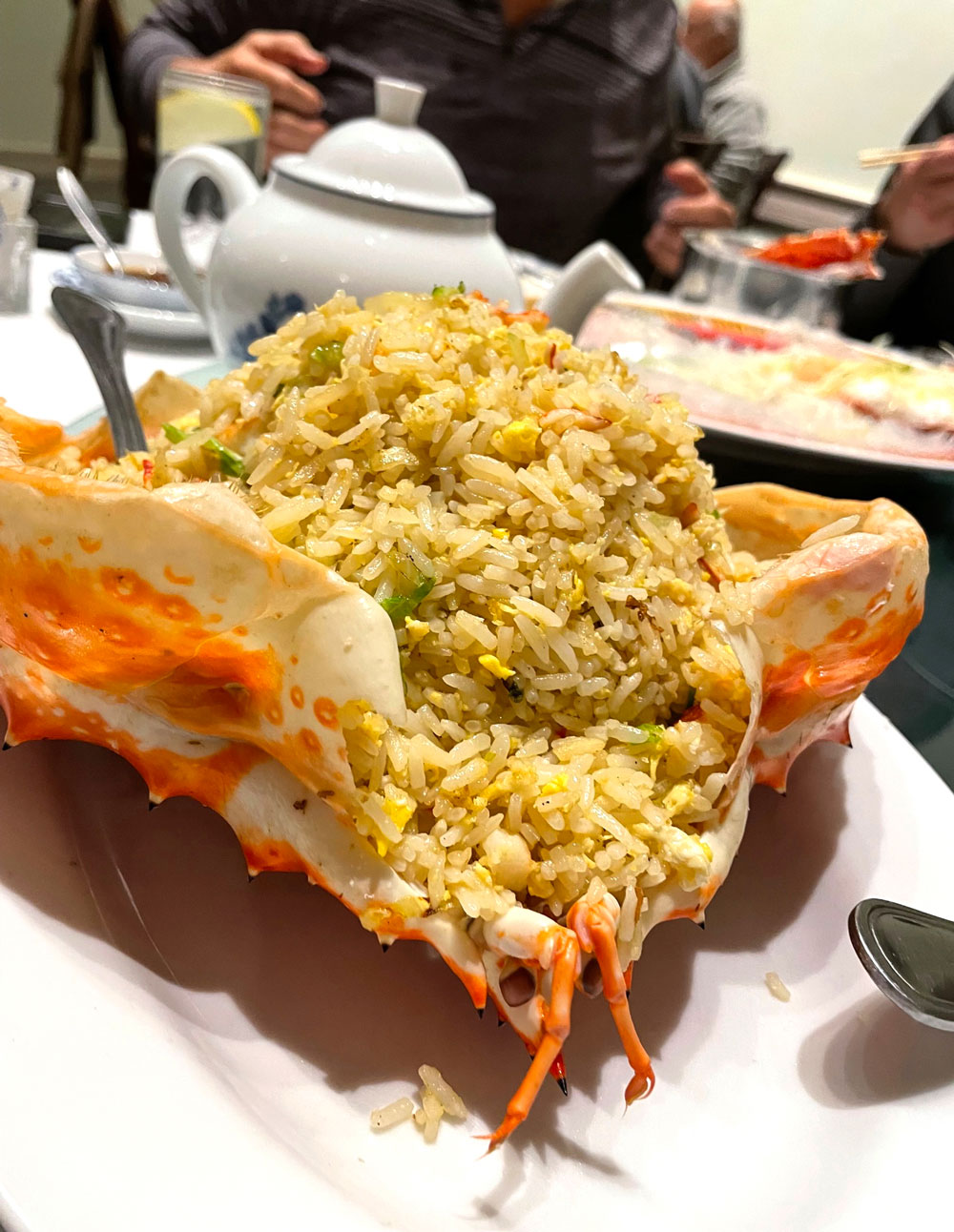 An image of King Crab Fried Rice in the shell of the crab, with people eating in the background.