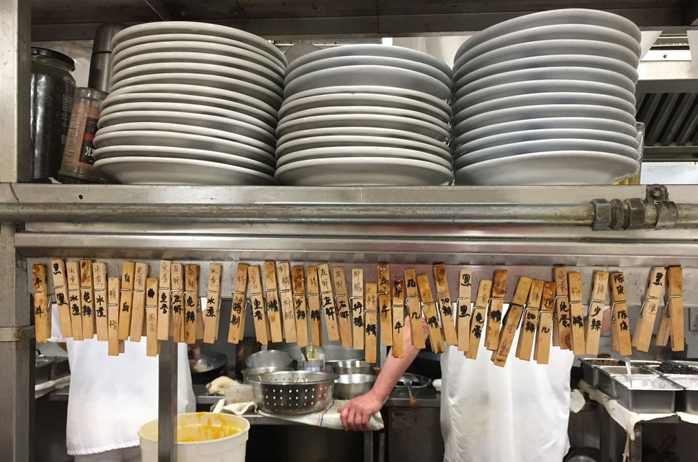 An image of a row of clothespins with Chinese characters on them inside Su Chang's kitchen--used to identify dishes and how they are cooked.