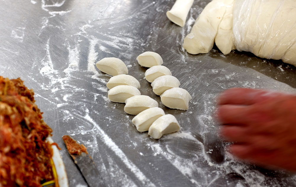 An image of peking ravioli (dumplings) being prepared in the kitchen using flour, dough, and stuffing.