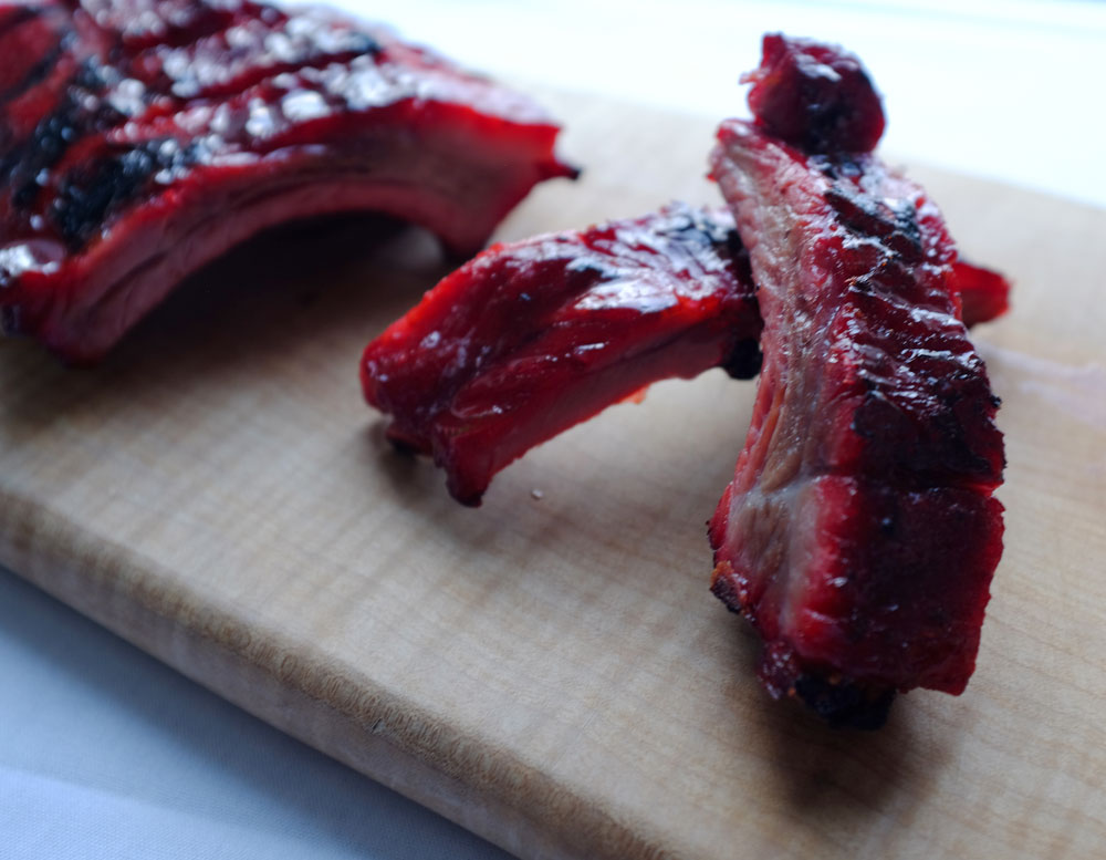 An image of a rack of barbecued spare ribs on a wooden cutting board, with two ribs stacked to the right in an 'x' formation.