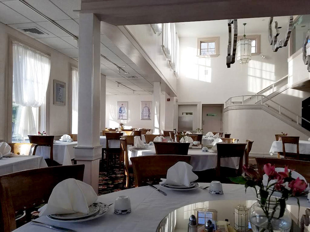 An image of the back dining room, sunlit, with a stairwell leading upstairs.